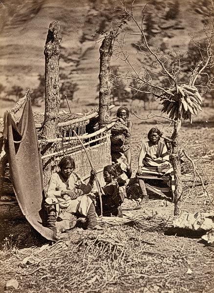 Navajo Daily LifeTimothy H. O’Sullivan captured some of the traditional daily life among the Navajo in this 1873 photo taken near Old Fort Defiance in New Mexico of Navajos clustered around a loom, hunting equipment and drying maize.– Courtesy Library of Congress –