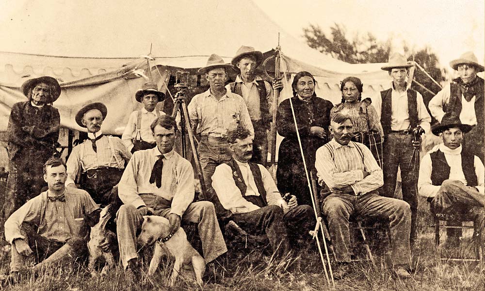 Holding a transit, rod and stakes, this allotment crew stood ready to divide land in Pine Ridge, in the newly formed South Dakota, circa 1890s. They were surrounded by, at far right, interpreter Billy Garnett (son of Fort Laramie Gen. Richard B. Garnett and Sioux mother Looks-At-Him), with wife Filla Janis, daughter and three sons. Also shown is John Brennan, wearing a stand up celluloid collar at far left, with son Paul behind him in the doorway; Brennan was probably working as South Dakota railway commissioner, as he wouldn’t become the agent at Pine Ridge until 1900. – All images courtesy Denver Public Library unless otherwise noted –